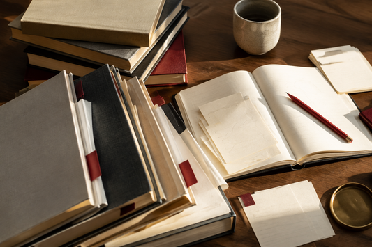Curated books, reading notes, and red pencil arranged on a warm wooden table